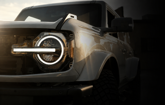 Ford Bronco in warm golden-hour light, shown from the front with rugged off-road tires and LED headlights.